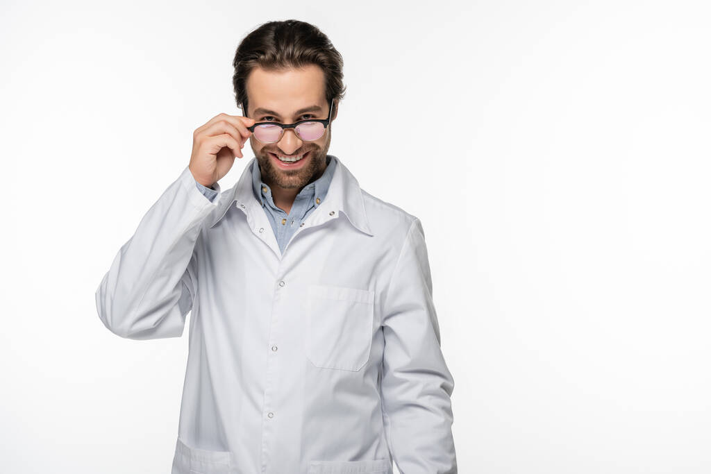 Médico sonriente sosteniendo anteojos aislados en blanco  - Foto, imagen