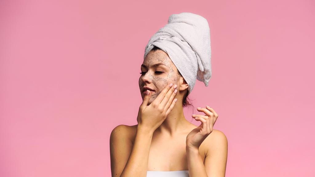 positive Frau trägt Gesichtsmaske auf, während sie isoliert auf rosa wegschaut - Foto, Bild