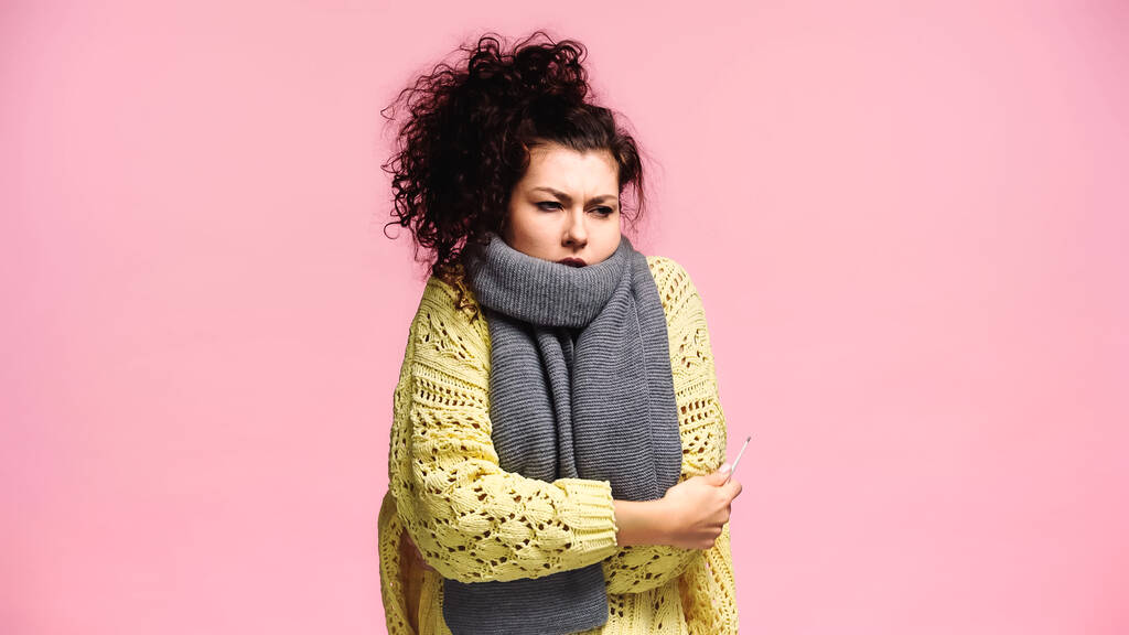 chora kobieta w ciepłym swetrze i szaliku z termometrem izolowanym na różowo - Zdjęcie, obraz