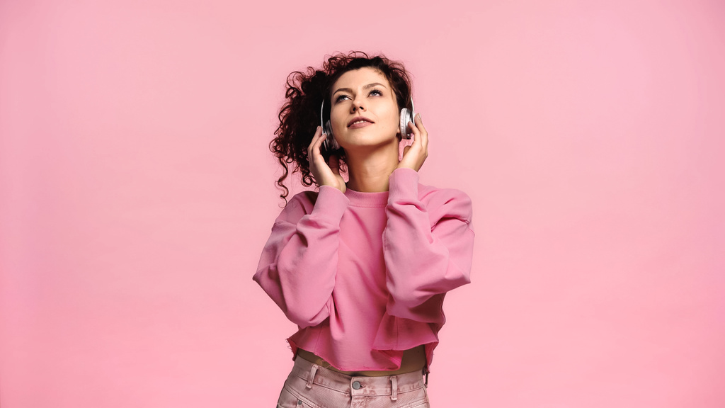 νεαρή γυναίκα κοιτάζει ψηλά και χαμογελά ακούγοντας μουσική απομονωμένη στο ροζ - Φωτογραφία, εικόνα