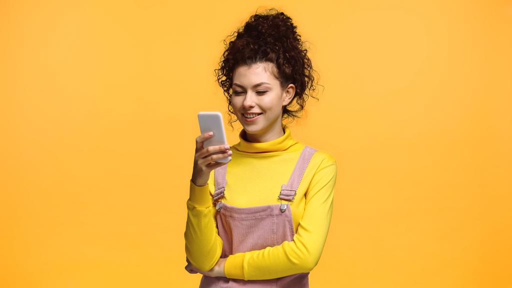 glimlachende brunette vrouw messaging op mobiele telefoon geïsoleerd op oranje - Foto, afbeelding