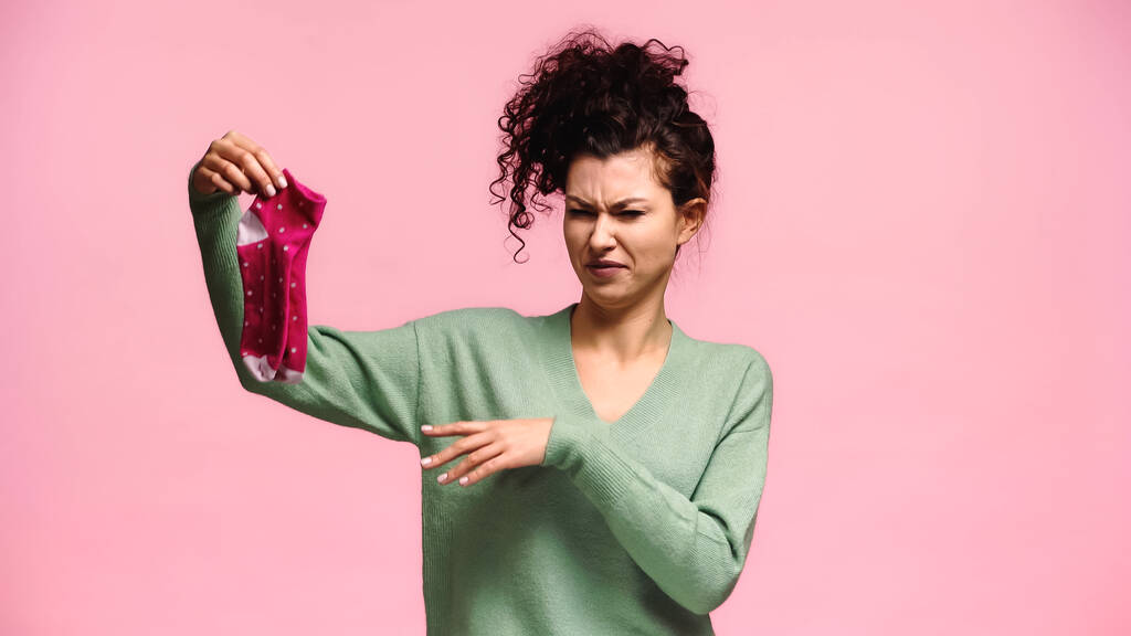 displeased woman pointing at stinky socks and grimacing isolated on pink - Photo, Image