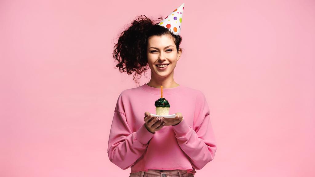 donna eccitata con cupcake di compleanno sorridente alla fotocamera isolata su rosa - Foto, immagini