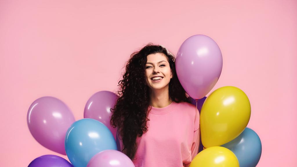 donna felice con palloncini multicolori sorridenti alla macchina fotografica isolata su rosa - Foto, immagini