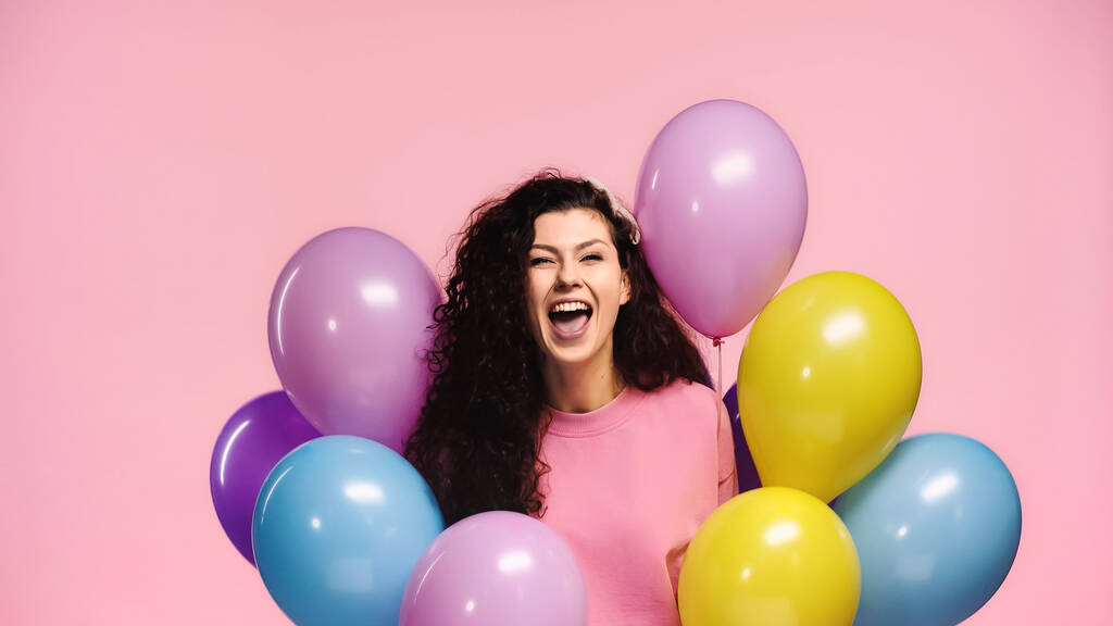 mujer llena de alegría con un montón de globos multicolores aislados en rosa - Foto, Imagen