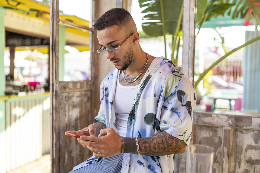 Una vista laterale di un giovane maschio barbuto spagnolo attraente in abiti eleganti digitando sul suo telefono - Foto, immagini