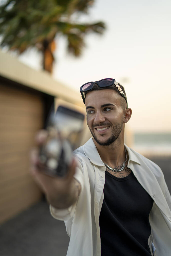 Un jeune homme barbu espagnol attrayant en vêtements élégants prenant un selfie avec un smartphone - Photo, image