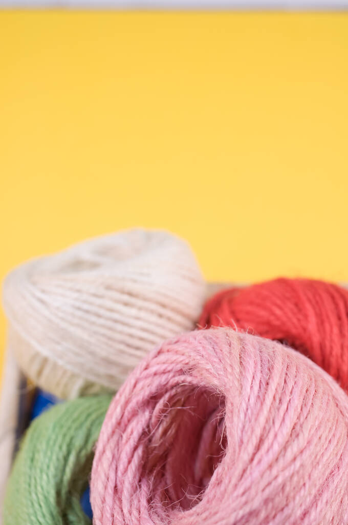 A vertical shot of colorful yarns on a box isolated on yellow background - Photo, Image