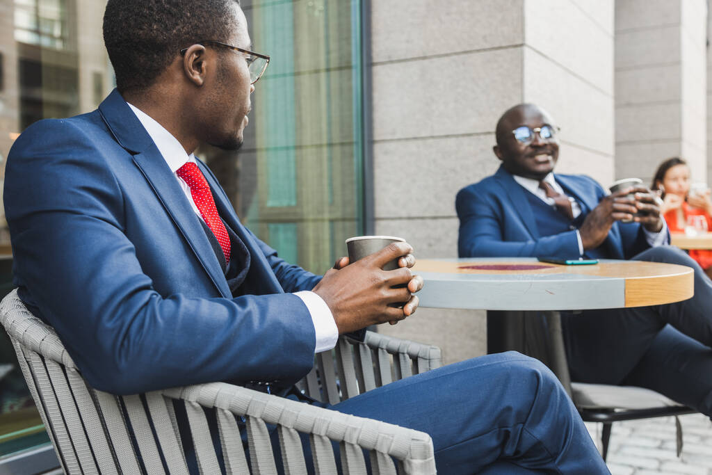 Spotkanie dwóch długoletnich przyjaciół czarnego Afroamerykanina biznesmena w garniturach na świeżym powietrzu w letniej kawiarni miejskiej - Zdjęcie, obraz