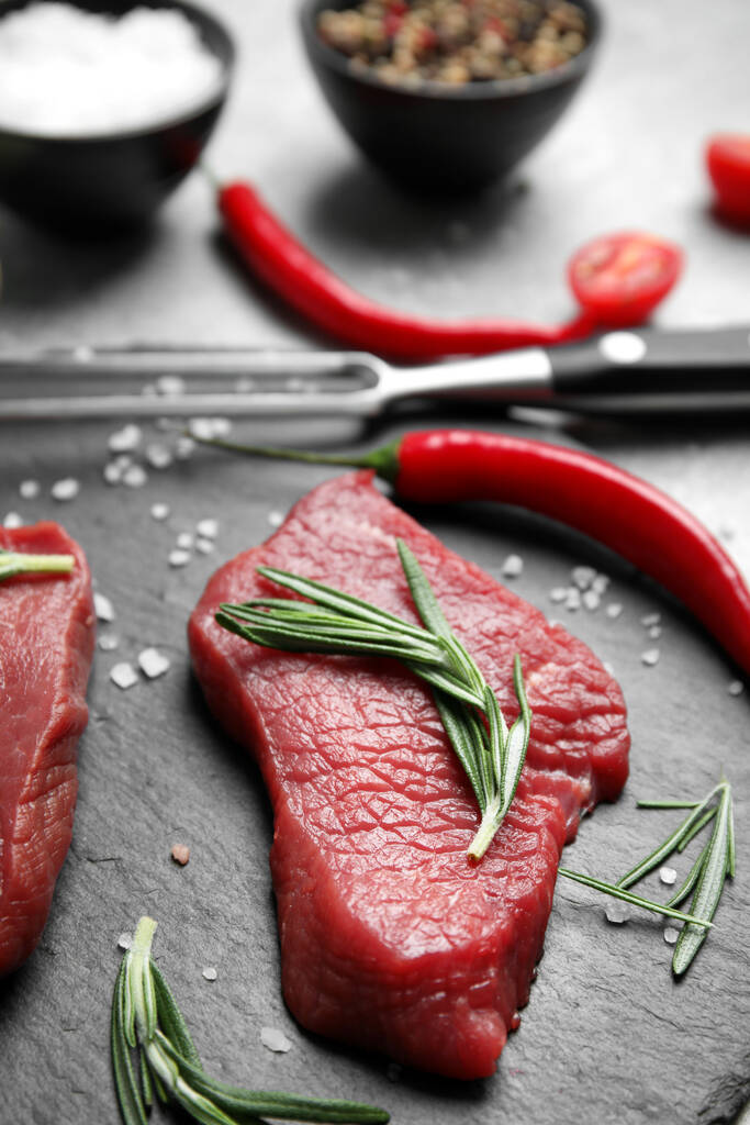Vers rauw vlees steaks en specerijen op leisteen plaat, close-up - Foto, afbeelding