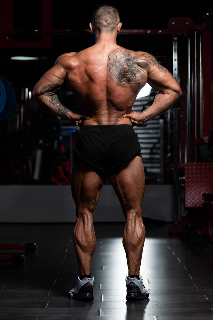 Fešák stojí silný v tělocvičně a pružné svaly - svalnatý atletický kulturista fitness model pózu po cvičení - Fotografie, Obrázek