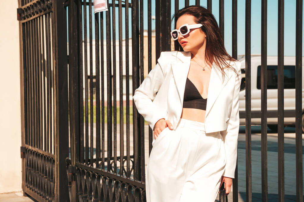 Portrait of young sexy modern businesswoman model. Hot beautiful woman in white suit posing on the street background. Fashion female walking outdoors in sunglasses - Photo, Image
