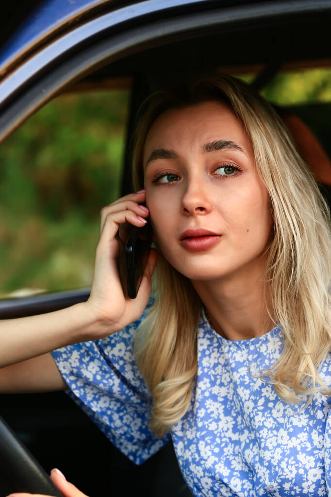 Junge Frau telefoniert mit Handy, während sie im Auto auf dem Fahrersitz sitzt. Attraktive blonde Studentin - Foto, Bild
