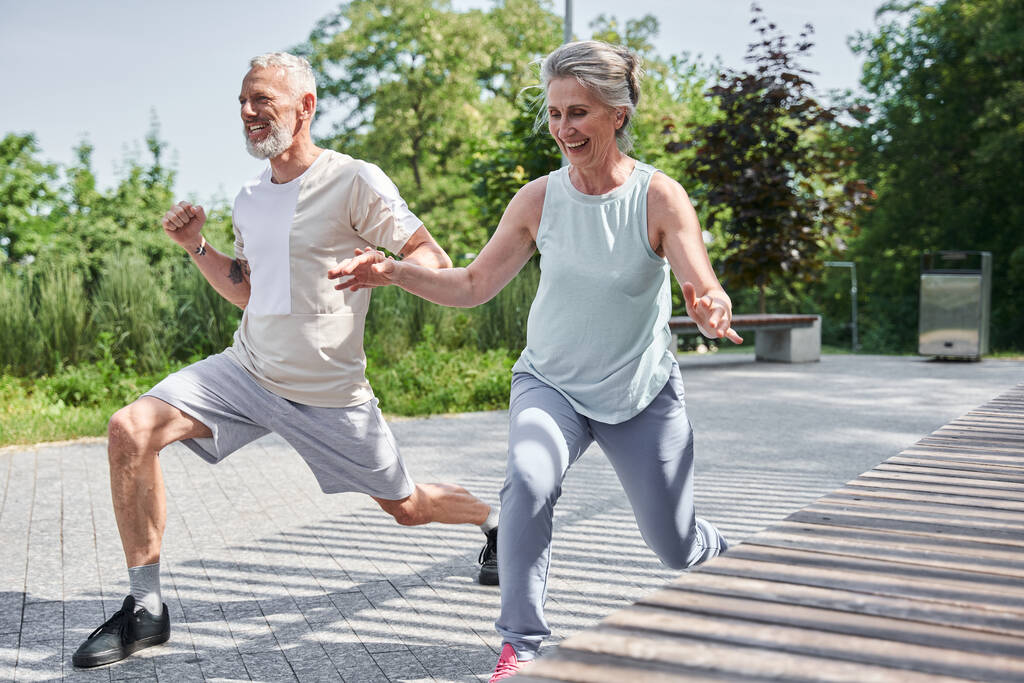 Senior married couple making lunges while training at the morning at the fresh air - Foto, Imagem
