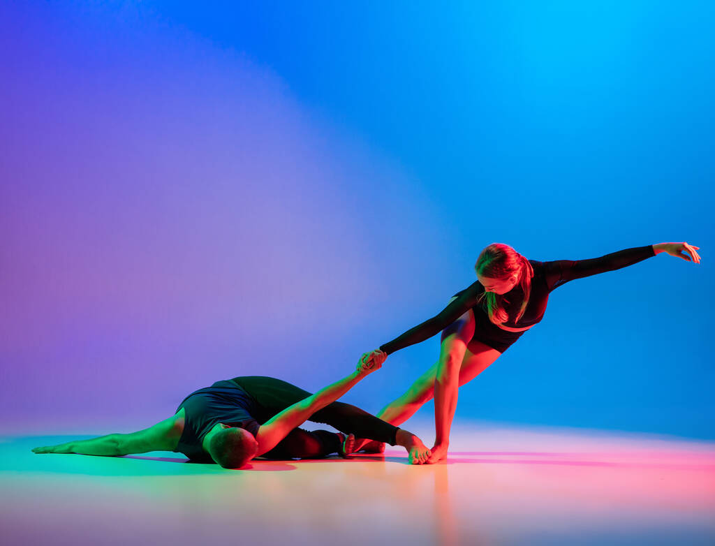 Elegante pareja deportiva caucásica, bailarina masculina y femenina bailando danza contemporánea sobre colorido degradado fondo rosa azul en luz de neón. - Foto, Imagen