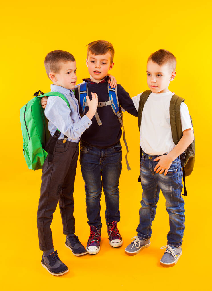 Lindos colegiales en uniforme con mochilas sobre fondo amarillo - Foto, Imagen