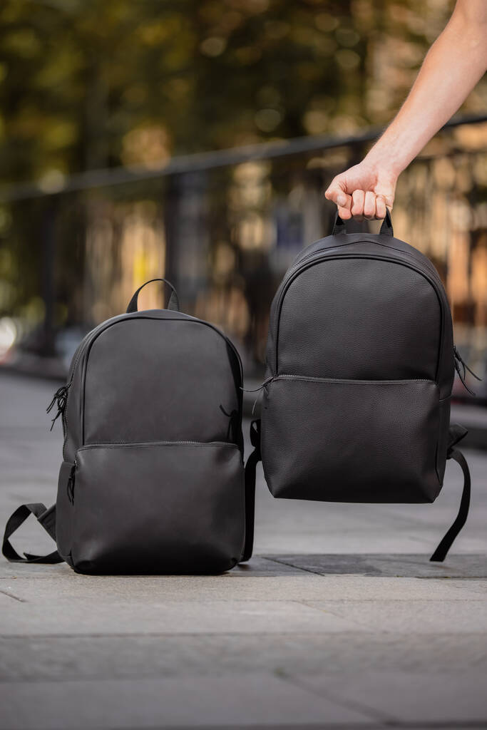 Два черных кожаных рюкзака и мужская рука держит один из них - Фото, изображение