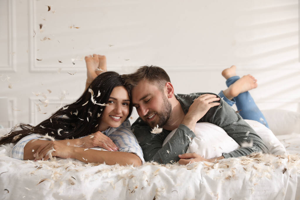 Щаслива молода пара відпочиває після веселого бою подушкою в спальні
 - Фото, зображення