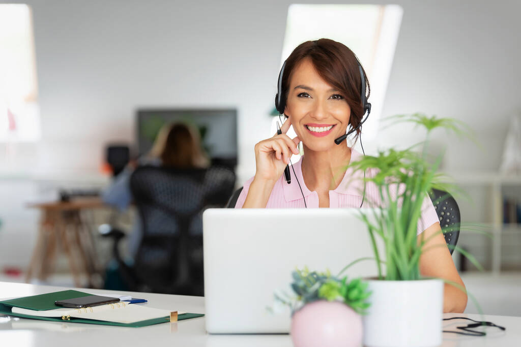 Asistente de servicio al cliente que usa auriculares mientras está sentada detrás de su computadora y trabaja en el centro de llamadas.  - Foto, imagen