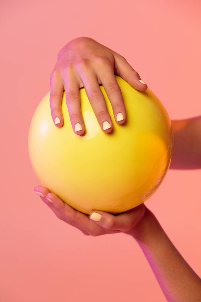 Primo piano mani femminili e ginnastica ritmica palla gialla isolato su sfondo rosa studio sfumato giallo con filtri al neon. - Foto, immagini