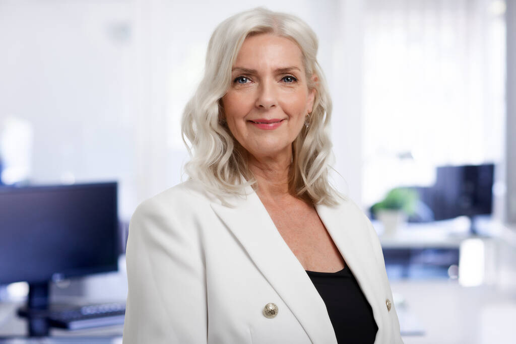 Portret van een mooie grijze harige senior zakenvrouw die op kantoor staat terwijl ze naar de camera kijkt en glimlacht.  - Foto, afbeelding