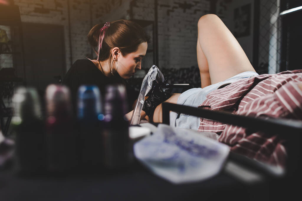 Profesyonel kadın dövme sanatçısı stüdyoda dövme yapıyor, yakın plan. Karanlık fotoğrafçılık - Fotoğraf, Görsel