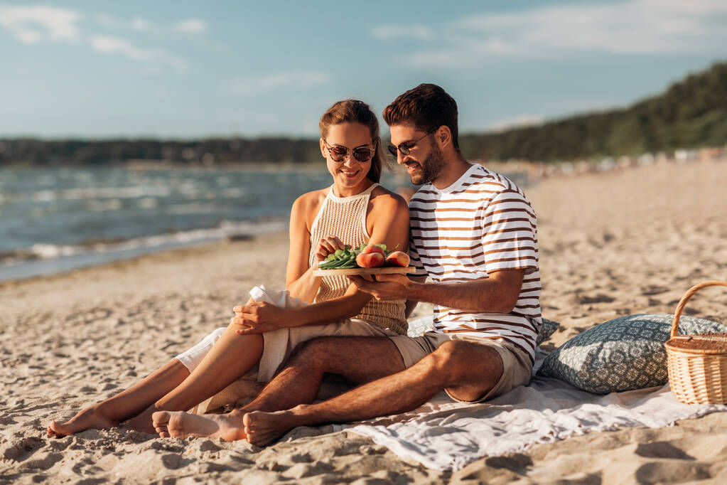 szczęśliwy para z jedzenie mając piknik na plaży - Zdjęcie, obraz