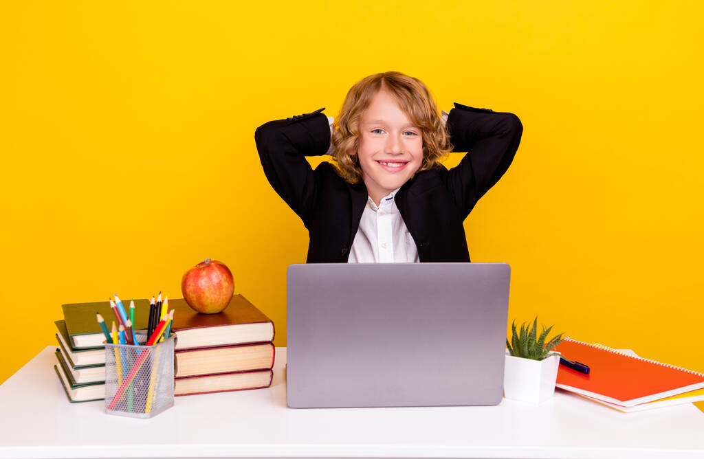 Foto van ontspannen schoolkind zitten bureau genieten van comfortabele break rest slijtage uniform geïsoleerde gele kleur achtergrond - Foto, afbeelding