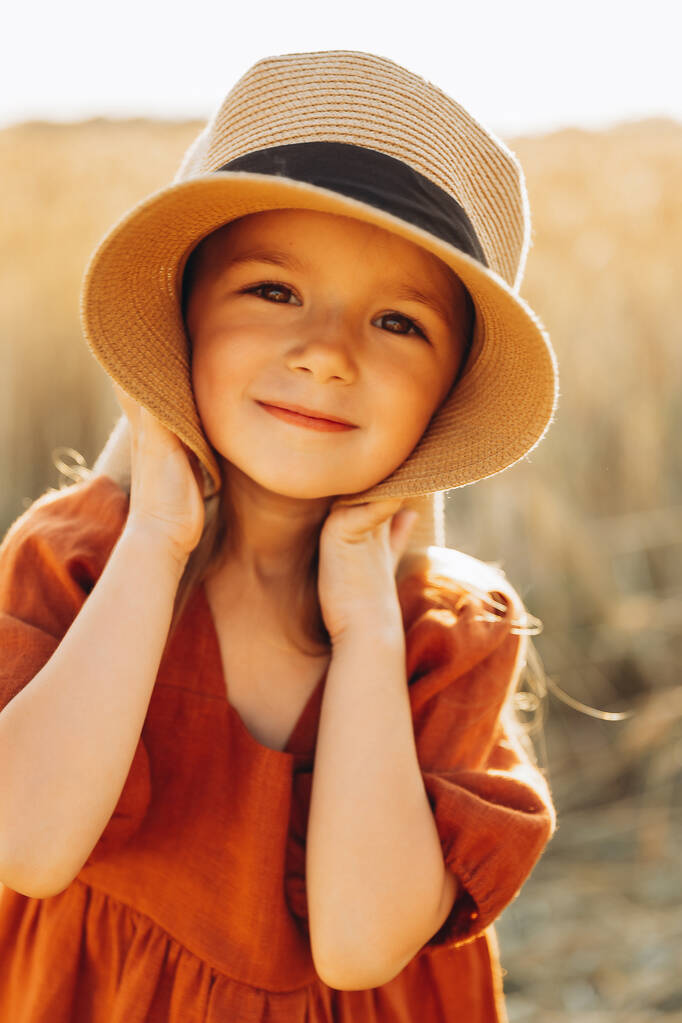 hezká 3-letá dívka chodí a pózuje na fotografii v pšeničném poli při západu slunce - Fotografie, Obrázek