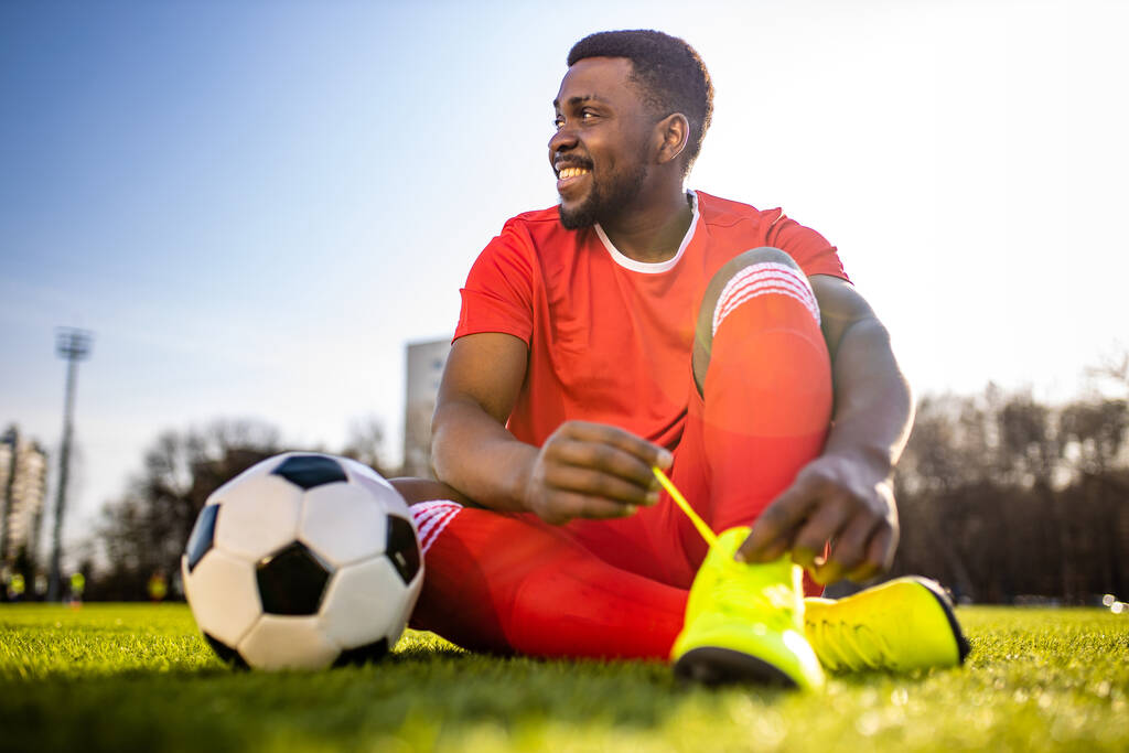 щасливий мультикультурний іспаномовний футболіст посміхається і носить червоний спортивний костюм на відкритому повітрі сонячний день
 - Фото, зображення