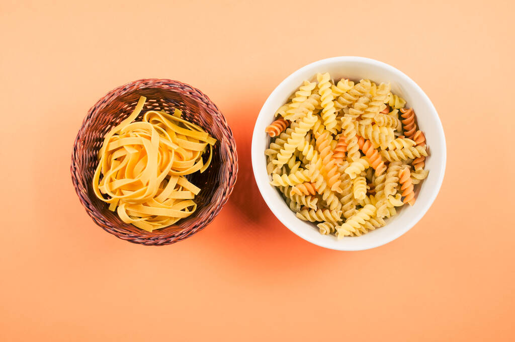 Eine Draufsicht auf dreifarbige Rotini und fettuccine Pasta auf einer Schüssel auf orangefarbenem Hintergrund - Foto, Bild