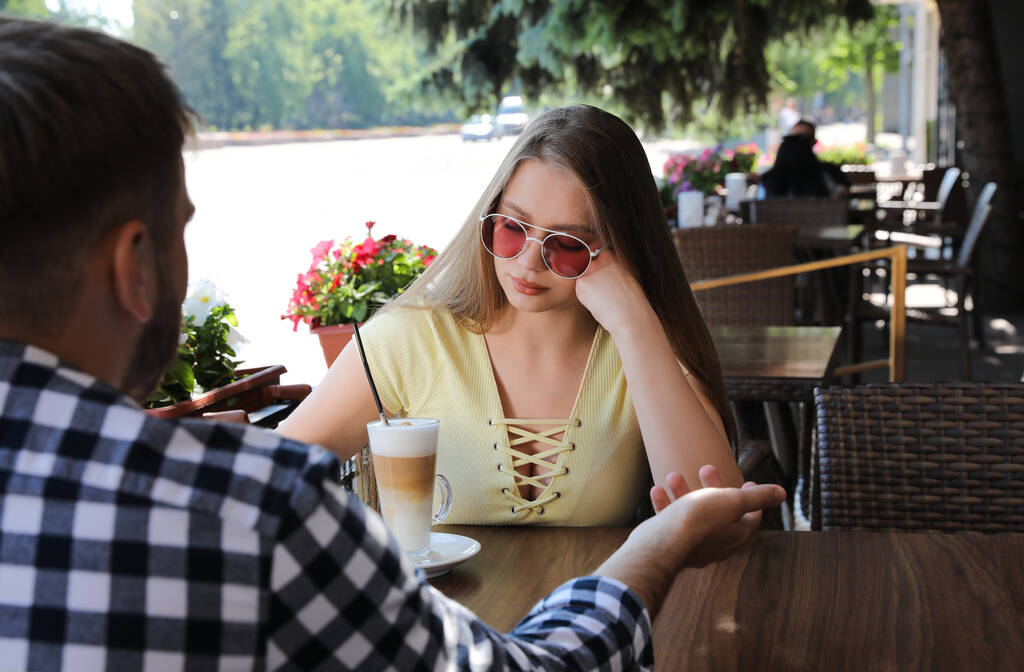 Νεαρή γυναίκα που έχει βαρετό ραντεβού με τον άντρα στην υπαίθρια καφετέρια - Φωτογραφία, εικόνα