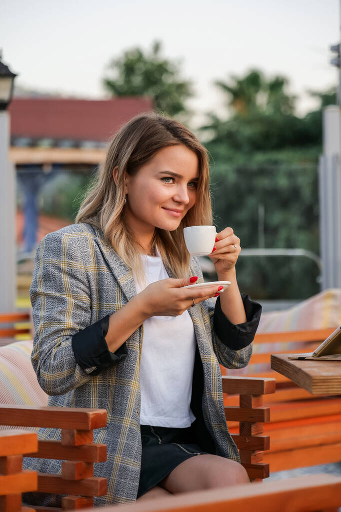 Charmante junge Geschäftsfrau sitzt mit einer Tasse Kaffee am Tisch - Foto, Bild