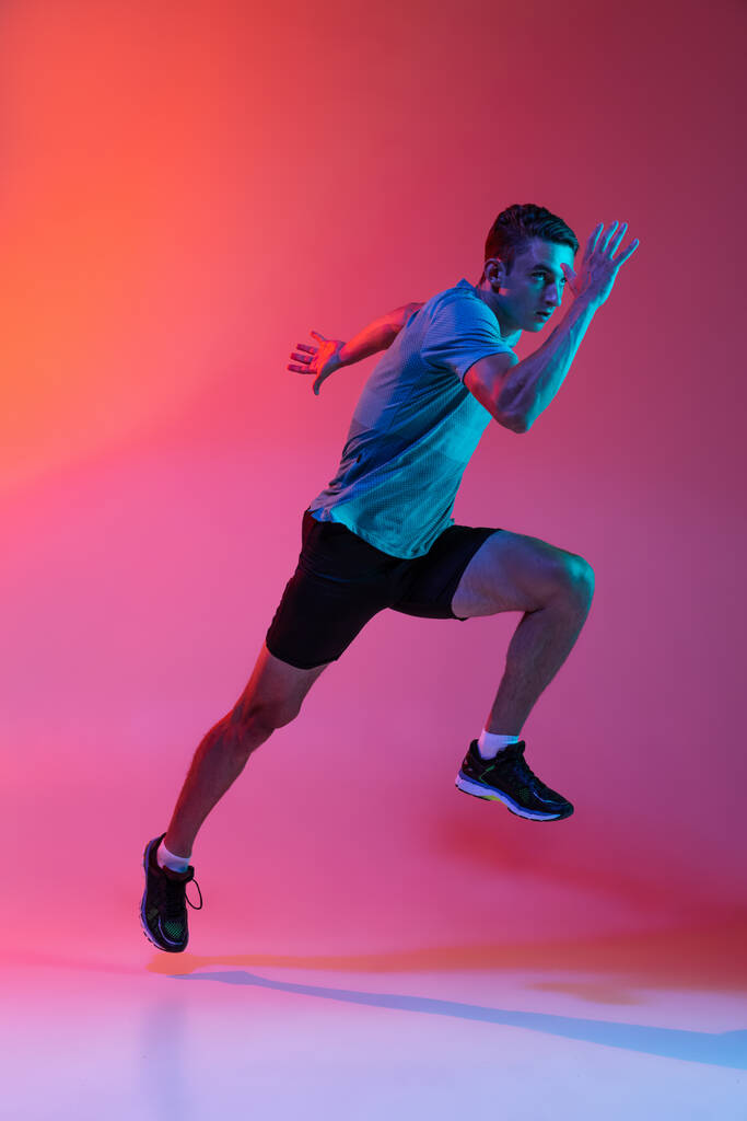 Portrat of Caucasian professional male athlete, runner training isolated on pink studio background with blue neon filter, light. Muscular, sportive man. - Photo, Image