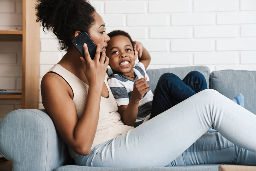 Musta nainen puhuu kännykkään halatessaan poikaansa kotona - Valokuva, kuva