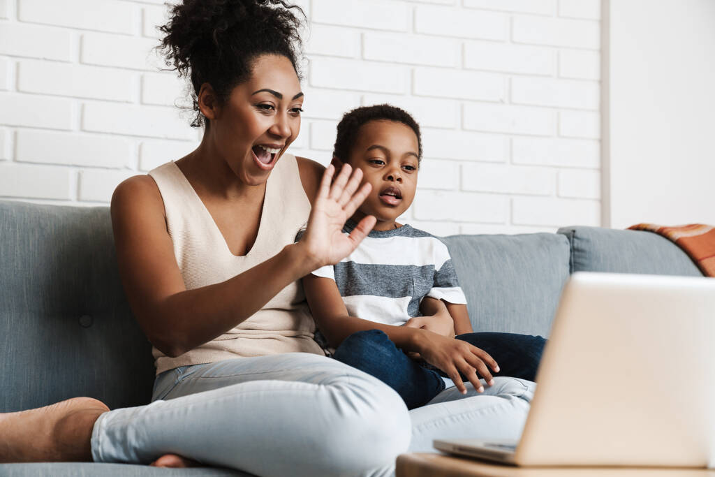 zwart gelukkig moeder en zoon gebaren terwijl met behulp van laptop thuis - Foto, afbeelding