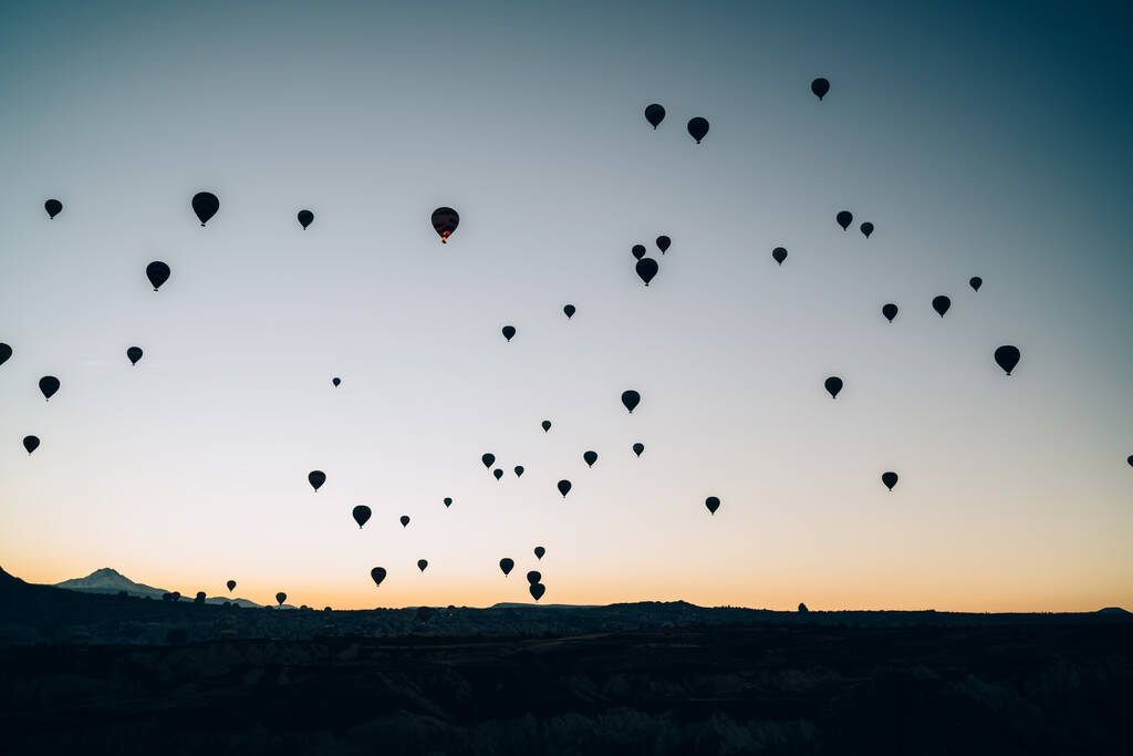 Schilderachtige landschap van veel zwarte lucht ballonnen silhouetten vliegen hoog boven de bergen tegen donkere zonsondergang hemel in de schemering tijd  - Foto, afbeelding