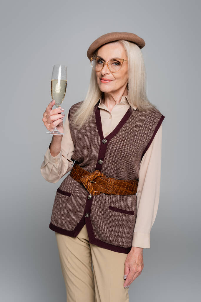 Senior vrouw in bril met glas champagne geïsoleerd op grijs  - Foto, afbeelding