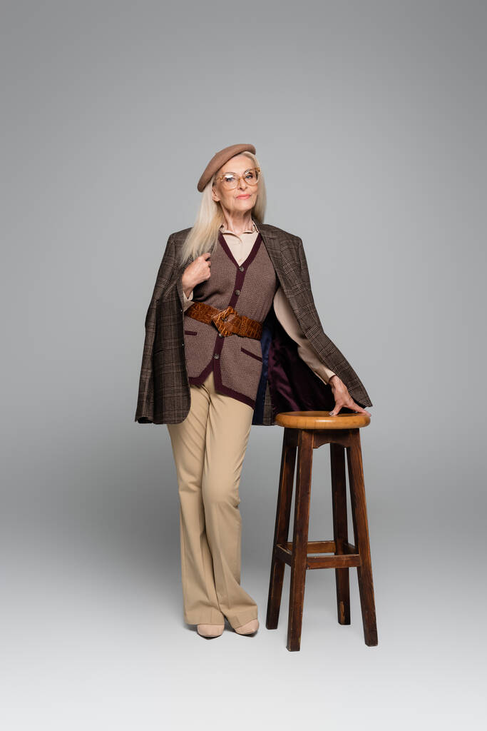 Stylish senior model posing near chair on grey background  - Photo, Image