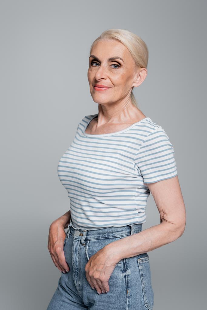 femme aux cheveux gris en t-shirt rayé posant avec les pouces dans des poches de jeans isolés sur gris - Photo, image