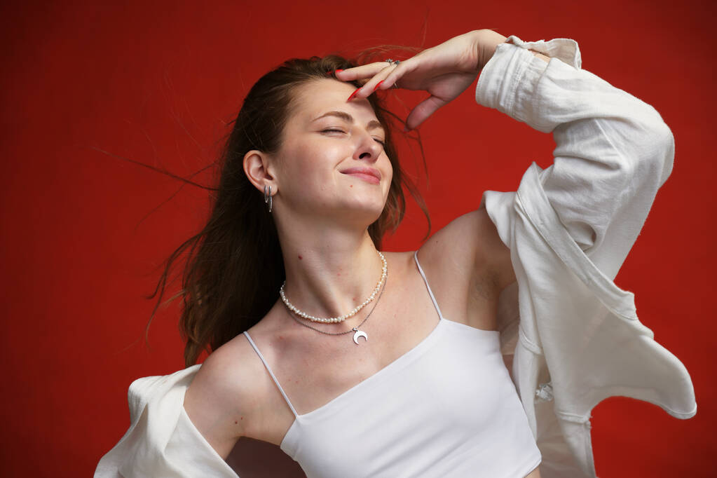 Modelo caucásico en camisa blanca muestra felicidad con una sonrisa sobre un fondo rojo - Foto, Imagen
