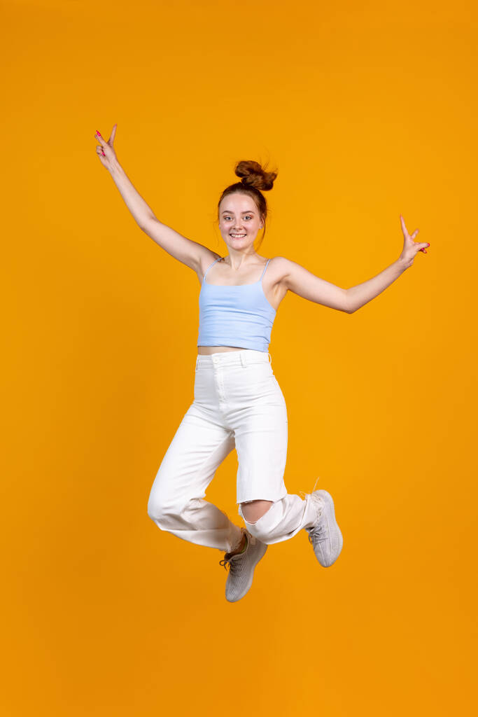 Vertical image of young cute girl jumping isolated on yellow studio background. Female fashion model in casual clothes. Concept of human emotions, natural beauty, youth - Photo, Image