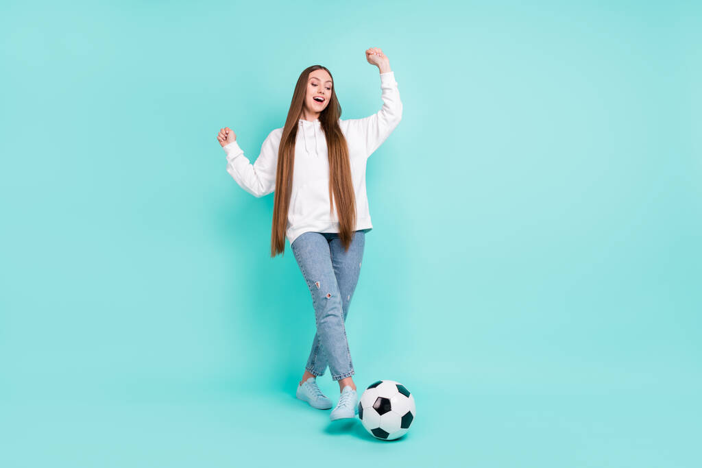 Foto de la afortunada joven brillante vestida con capucha blanca sonriente ganar partido de fútbol levantando puños aislados color verde azulado fondo - Foto, Imagen
