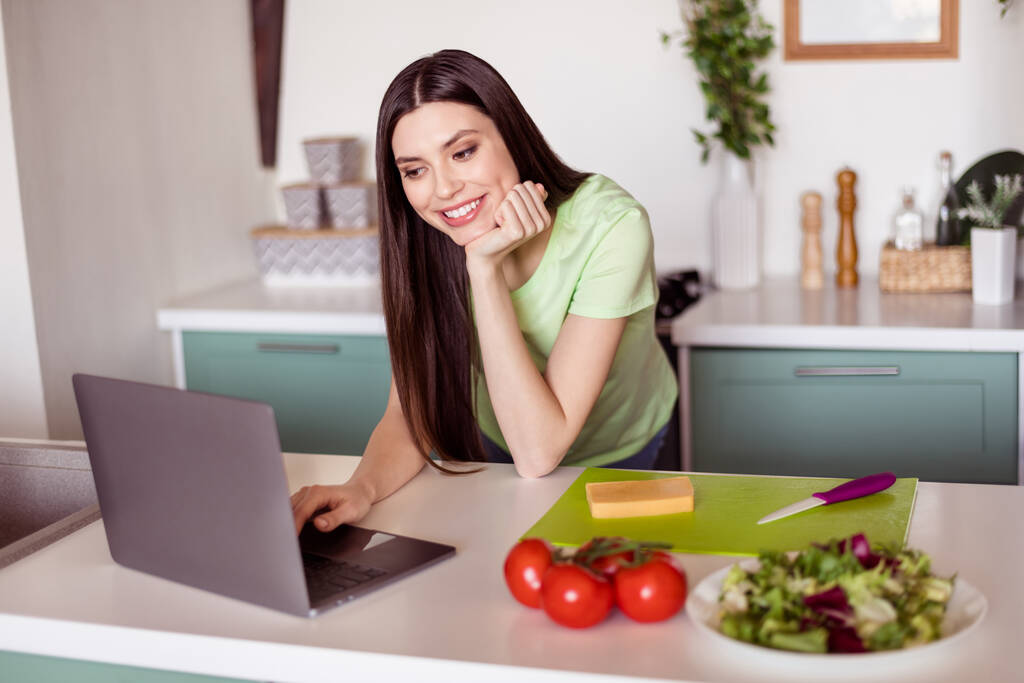 Yeşil tişörtlü, kahvaltı hazırlayan, ev içinde modern aletler yazan sevimli genç bir kadının fotoğrafı. - Fotoğraf, Görsel