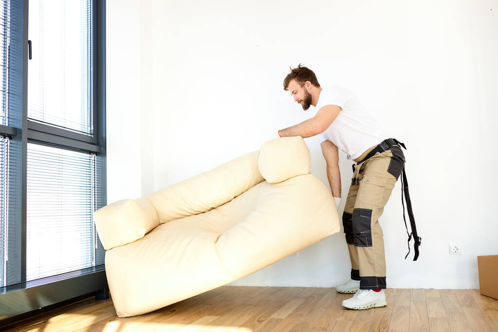 Concept de réinstallation. Portrait de réparateur masculin confiant déplaçant le canapé nouvel appartement - Photo, image