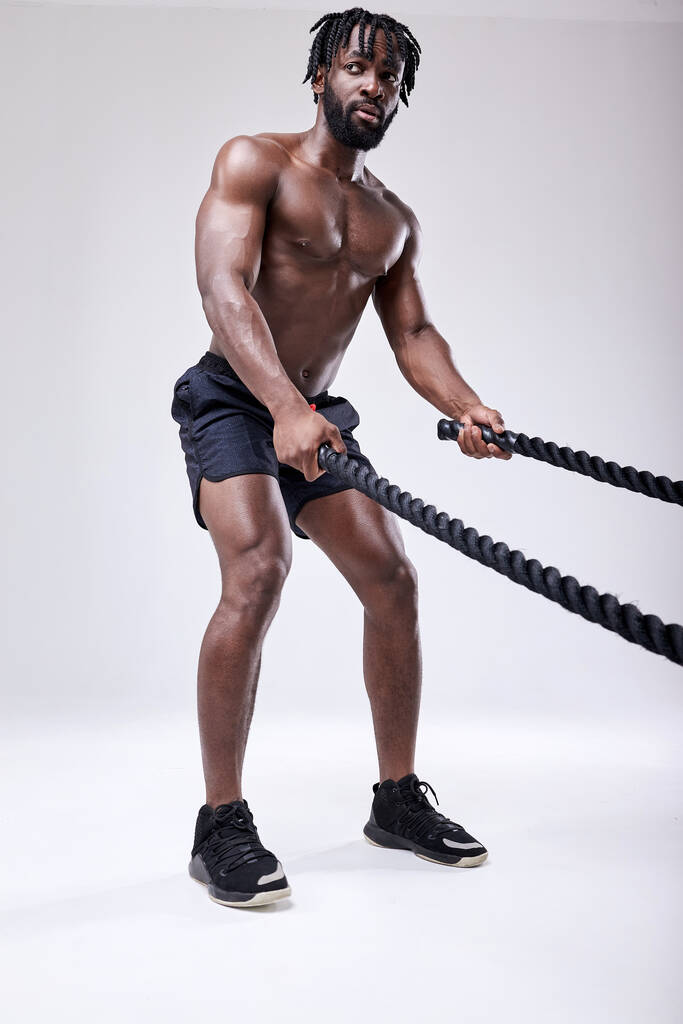 Zweterige Shirtless Afro Man Training met Battle Rope In Studio Op Witte Achtergrond - Foto, afbeelding