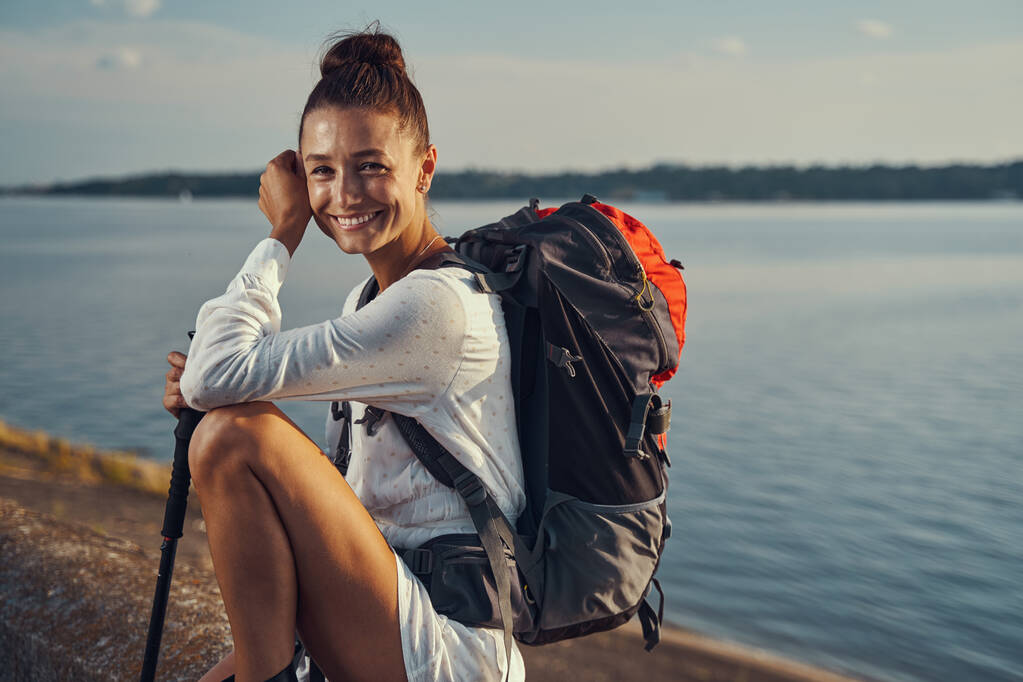Hiker smiling happily while sitting near lakeside - Photo, Image