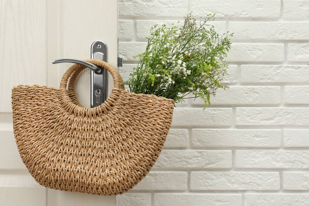 Κομψή τσάντα παραλίας με όμορφα αγριολούλουδα κρεμασμένη στο χερούλι της πόρτας. Χώρος για κείμενο - Φωτογραφία, εικόνα