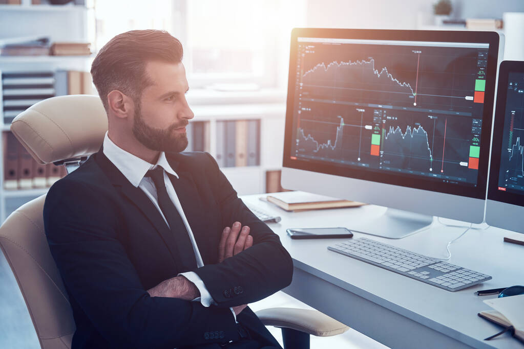 Huomaavainen nuori mies paidassa ja solmio analysoimalla tietoja osakemarkkinoilla työskennellessään toimistossa - Valokuva, kuva