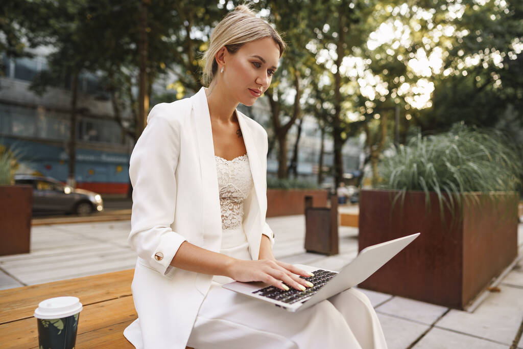 Joven mujer de negocios hermosa que trabaja en el ordenador portátil, sentado en el banco en la calle - Foto, imagen